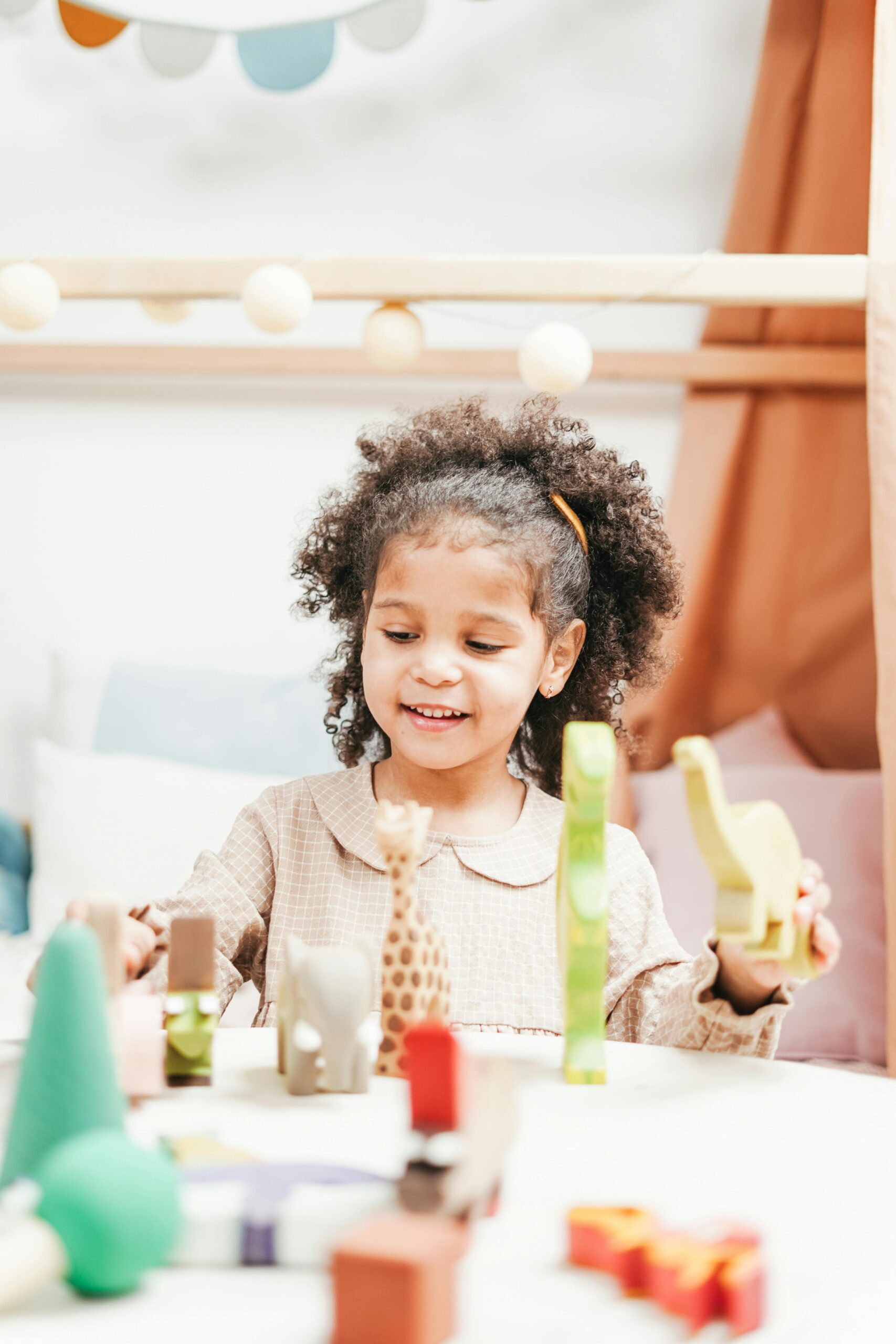 Smiling young girl enjoys playtime with wooden toys in a bright, cozy playroom.