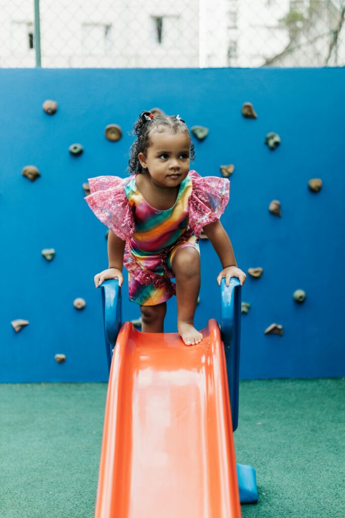 A joyful child in a colorful dress playing on a slide at a playground.