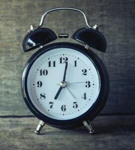 Classic black analog alarm clock on rustic wooden background, perfect for time and nostalgia themes.